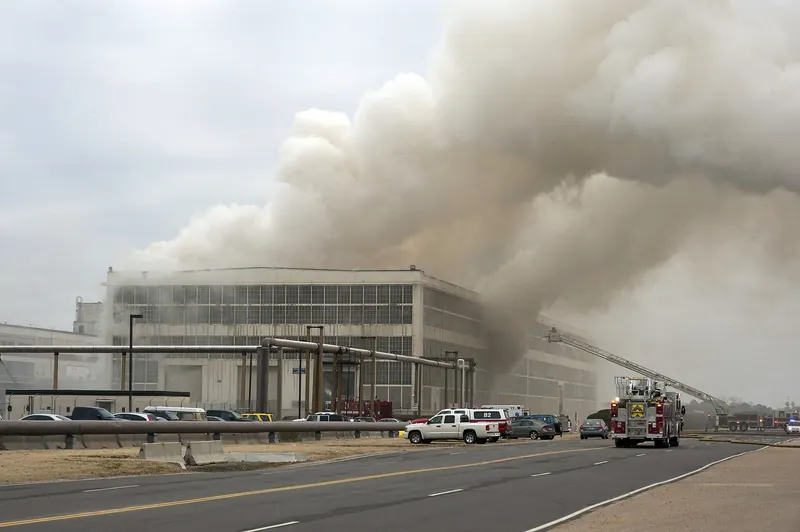 Heavy smoke rising from a large warehouse fire as fire apparatus respond
