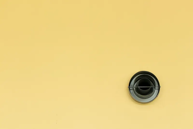 Round air vent diffuser set into a plain yellow wall