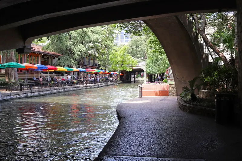 San Antonio River Walk with colorful café umbrellas seen from beneath a stone bridge