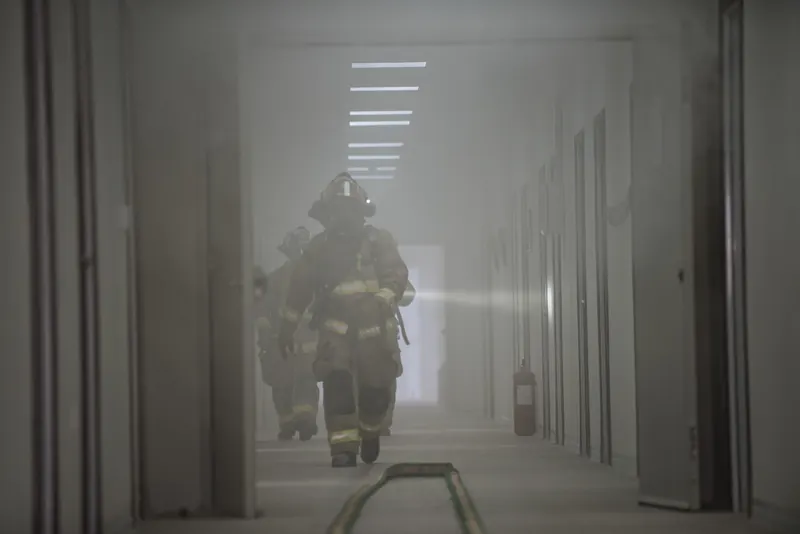 Firefighter walking down a long corridor filled with thick gray smoke