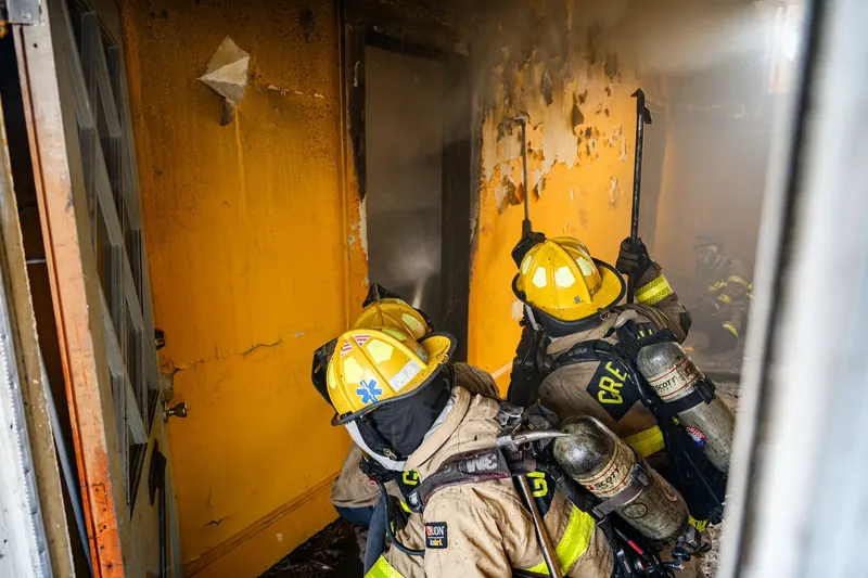 Firefighters inside a smoke-filled room with scorched, peeling paint on the walls
